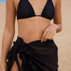 A woman in a black bikini and skirt poses on the beach, embodying a vibrant summer style.