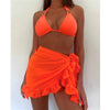 A woman wearing an orange bikini top and matching skirt stands confidently, showcasing a vibrant summer look.