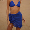 A woman in a blue bikini and skirt poses on the beach, embodying a vibrant summer style.