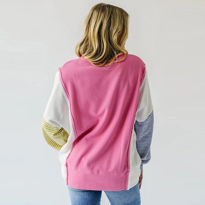 Pink and yellow striped sweatshirt displayed on a hanger against a neutral background.
